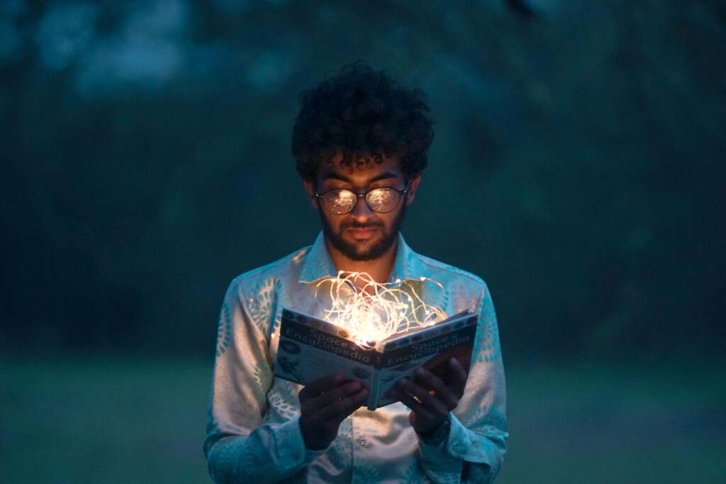 Hombre leyendo un libro del que sale luz, como si le transportase a lo que está leyendo